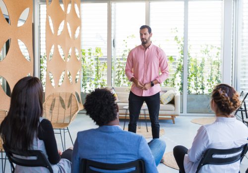 Serious confident male coach holding seminar. Young business man in casual speaking before audience. Seminar concept